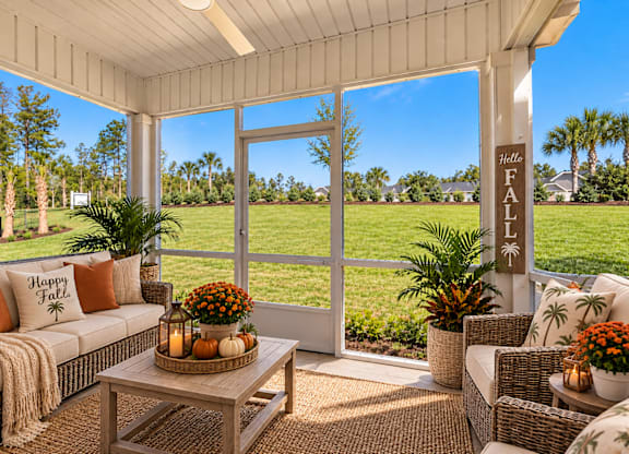 A sunny patio with a couch, pillows, and a sign that says "Happy Fall".