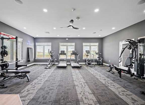 A spacious gym with a variety of equipment and a ceiling fan.