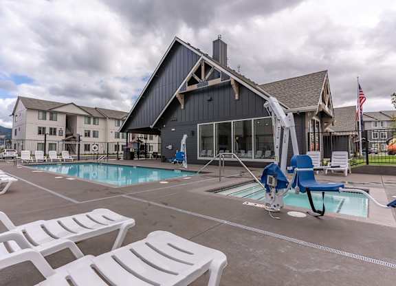 A large outdoor swimming pool with lounge chairs and a building in the background at Marcola Apartment Homes, Oregon