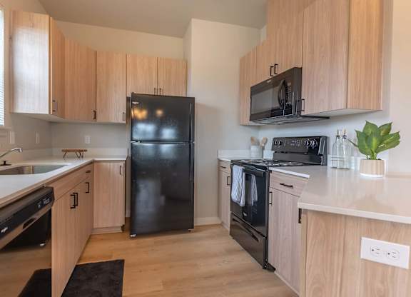 A kitchen with wooden cabinets and a black refrigerator at Marcola Apartment Homes, Oregon