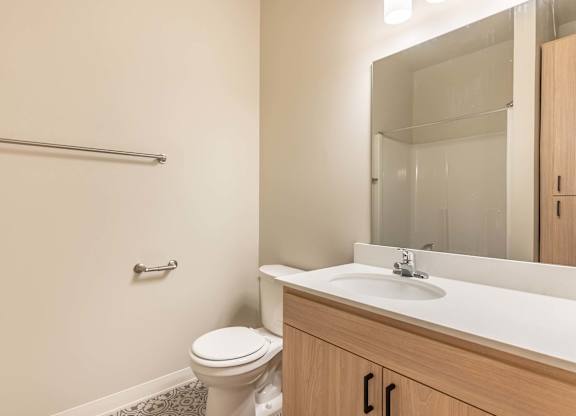 A bathroom with a toilet, sink, and mirror at Marcola Apartment Homes, Forest Grove
