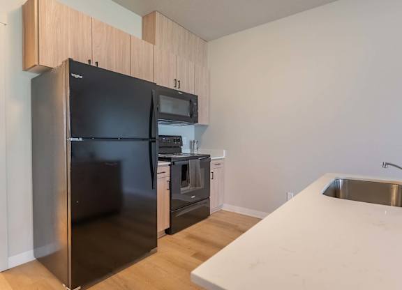 A black fridge and microwave in a kitchen with wooden cabinets at Marcola Apartment Homes, Forest Grove, Oregon