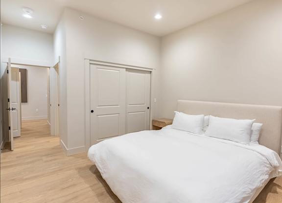 A white bed with a white headboard and two white pillows in a bedroom with wooden floors and white walls at Westgate Apartment Homes, Pendleton, Oregon