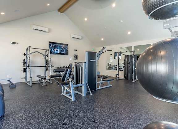 A spacious gym with a variety of equipment including a squat rack, bench, and a large exercise ball at Westgate Apartment Homes, Pendleton