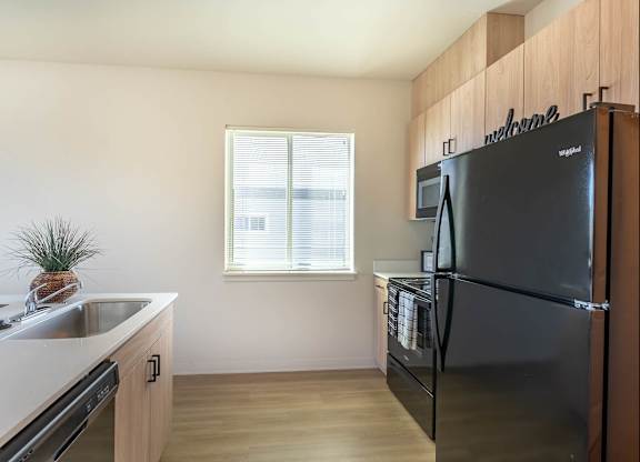 A kitchen with a black fridge and a window with blinds at Westgate Apartment Homes, Oregon