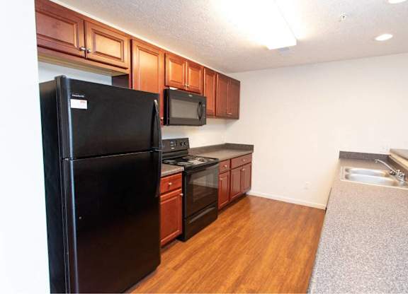 A black refrigerator is in a kitchen with wooden cabinets and a microwave.