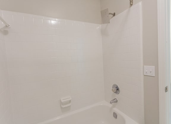 A white tiled shower with a white tub and a white shower head.