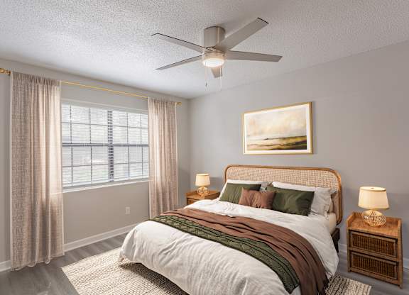 A bedroom with a large bed, a ceiling fan, and a painting on the wall.