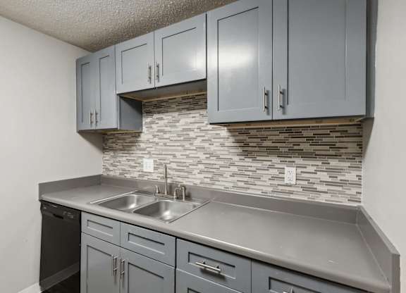 A kitchen with grey cabinets and a stone backsplash.