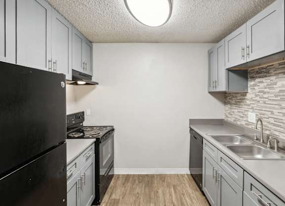 A kitchen with a black refrigerator and a stone backsplash.