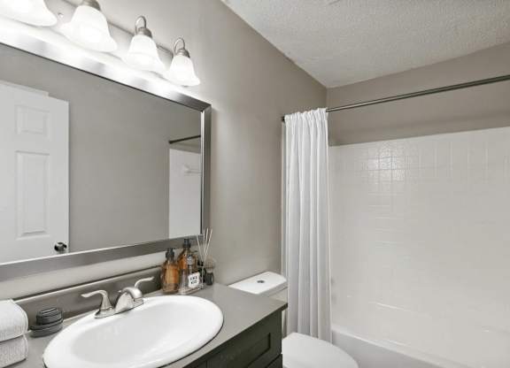 A white bathroom with a sink, mirror, and shower.