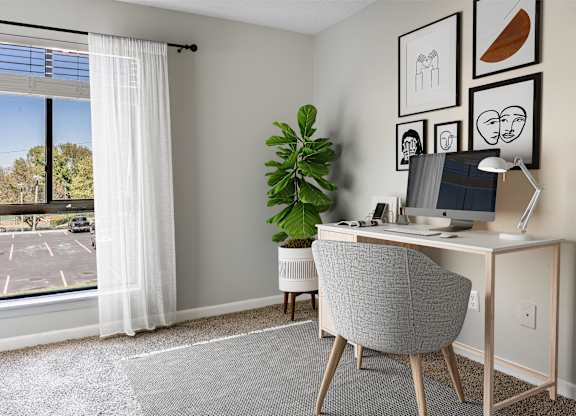 A room with a desk, chair, and a plant.