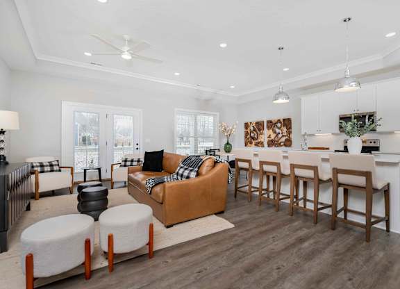 A modern living room with a brown sofa and a white kitchen in the background.