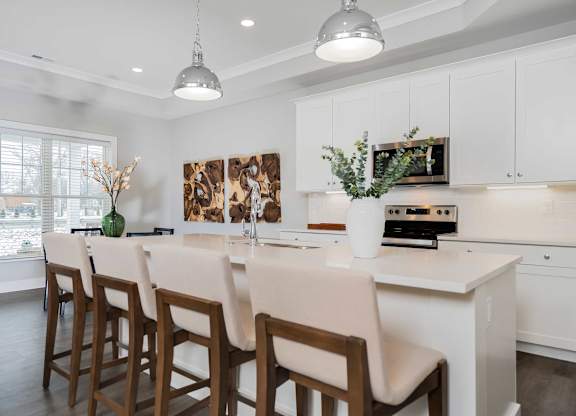 A kitchen with white cabinets and a large island with chairs around it.