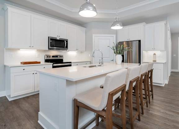 A kitchen with white cabinets and a long island with chairs.