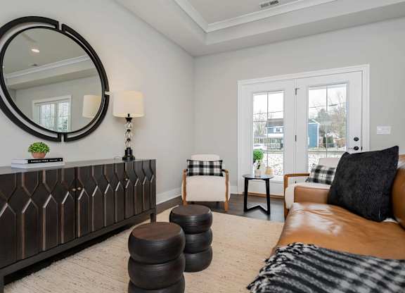 A living room with a brown leather couch and a round mirror on the wall.