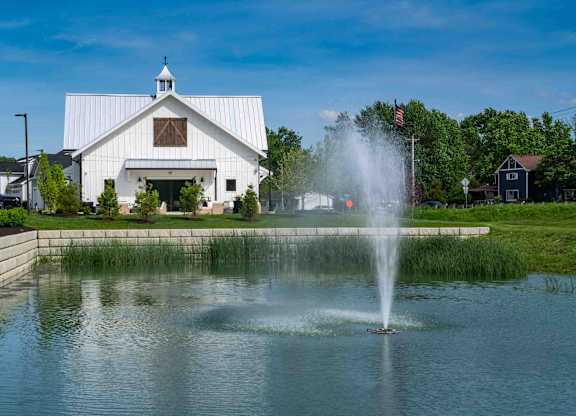 A white barn with a fountain in front of it.