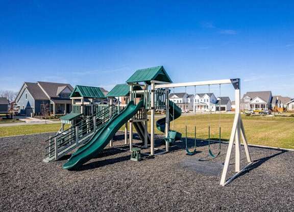 A playground with a green slide and a white swing set.