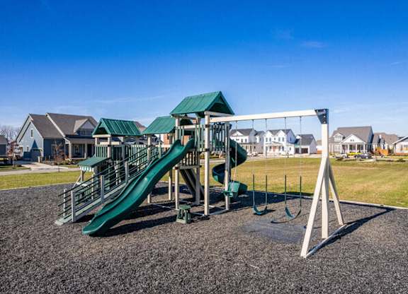 A playground with a green slide and a white swing set.