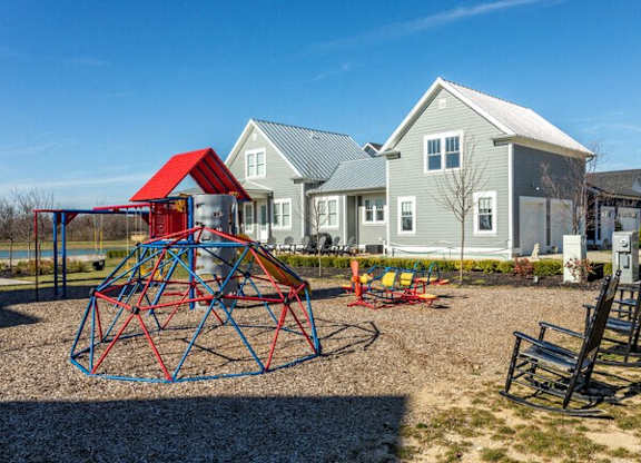 A playground with a red and blue swing set in front of a grey house.