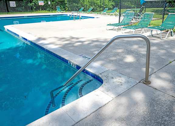 A pool with a metal ladder and green chairs at Sawbranch Apartments, Summerville 29485