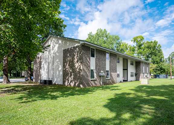 A house with a grey and white exterior is surrounded by a grassy lawn and trees at Sawbranch Apartments, Summerville, SC, 29485