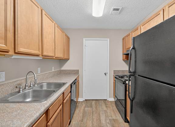 A kitchen with a black refrigerator and wooden cabinets at Sawbranch Apartments, Summerville, SC