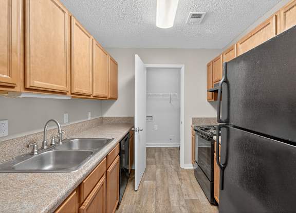 A kitchen with a black refrigerator, sink, and wooden cabinets at Sawbranch Apartments, Summerville