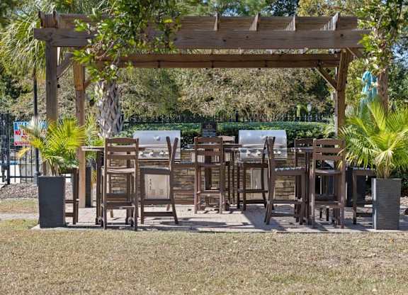 A wooden pergola with chairs and tables is surrounded by greenery at The Preserve at Pine Valley Apartments, North Carolina