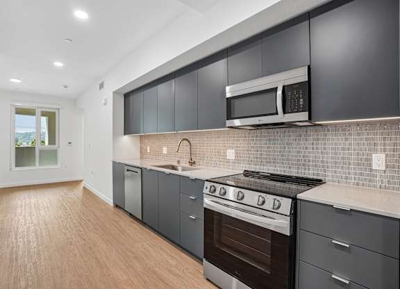 A modern kitchen with dark grey cabinets and stainless steel appliances.