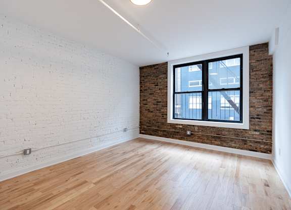 A room with a wooden floor and a window with a view of a building outside.
