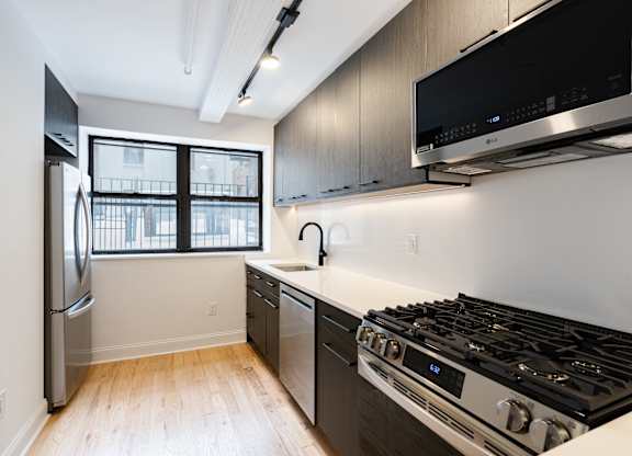 A modern kitchen with a stainless steel refrigerator, a stove, and a flat-screen TV mounted above the stove.