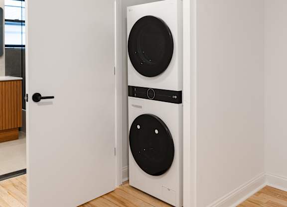 A white door is open to reveal a black washing machine and dryer.