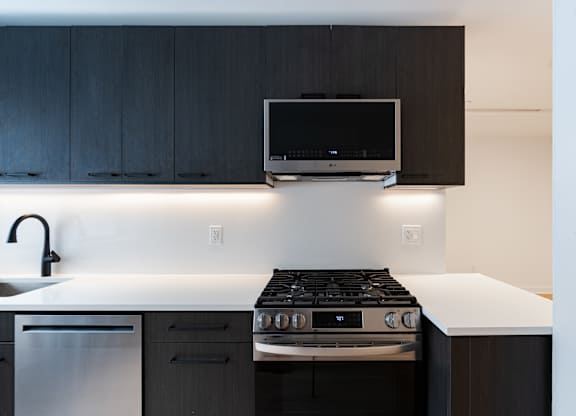 A modern kitchen with a black stove top oven and a flat screen TV mounted above the stove.