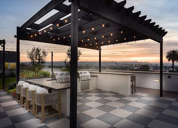 A patio with a bar and chairs under a pergola with lights.
