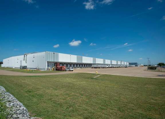 A large white building with a long row of windows and a truck parked in front.