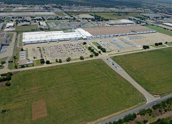 An aerial view of a large building complex surrounded by a parking lot and green fields.