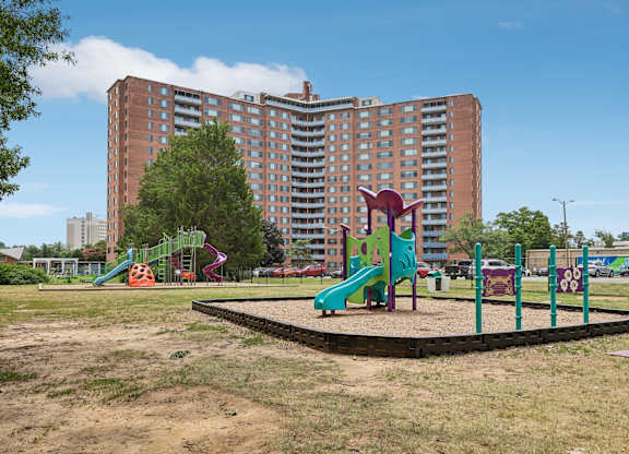 A playground with a green slide and a purple slide in front of a large apartment building.