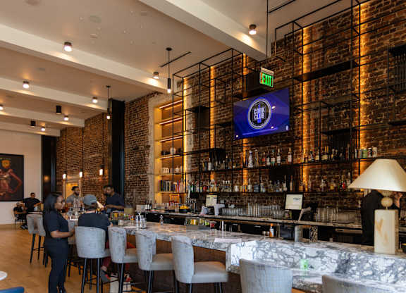 A bar with people sitting at the bar and a TV screen on the wall.