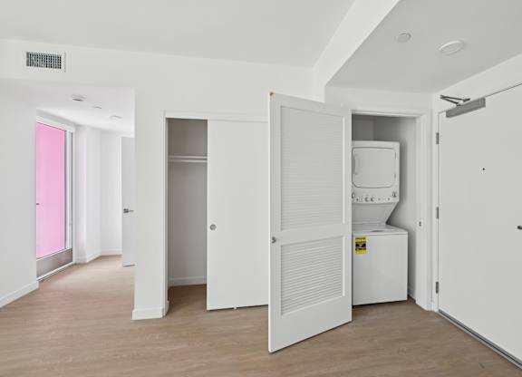 A white room with a pink door and a white fridge.