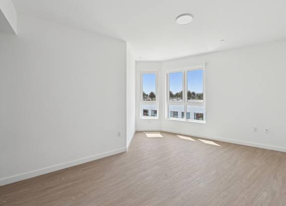 A room with white walls and wooden flooring, with a large window and pictures on the wall.