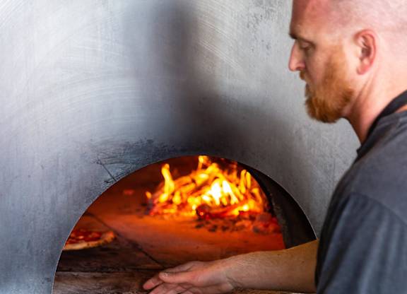 A man is making pizza in a wood-fired oven.at Channel House, Oakland, 94607