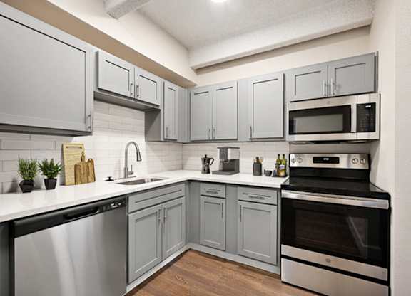 A kitchen with a stainless steel dishwasher and oven, and grey cabinets. at The Lex At Lowry, Denver, CO
