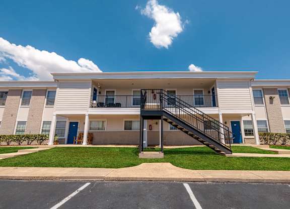 A large white apartment building with a black staircase leading to the entrance.