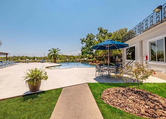 A pool area with a blue umbrella and a concrete walkway.