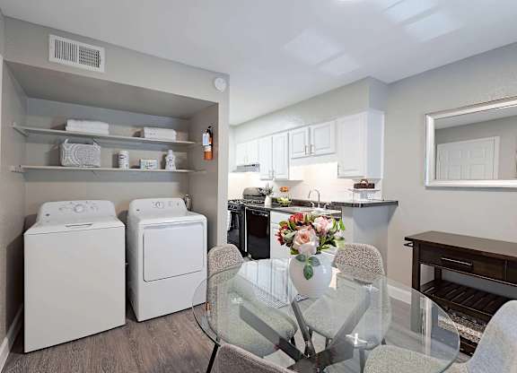 A laundry room with a washer and dryer, a dining table with chairs, and a kitchen area with cabinets and a countertop.