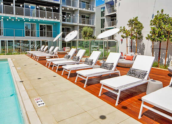 A row of sun loungers are set up on a wooden deck next to a pool.at Prizma, Los Angeles, 90038  