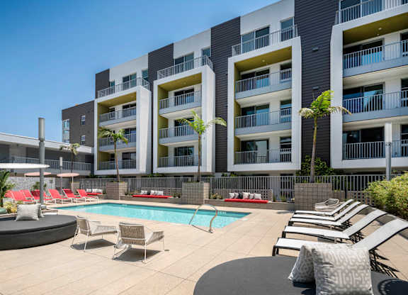 A modern apartment complex with a pool and lounge chairs.