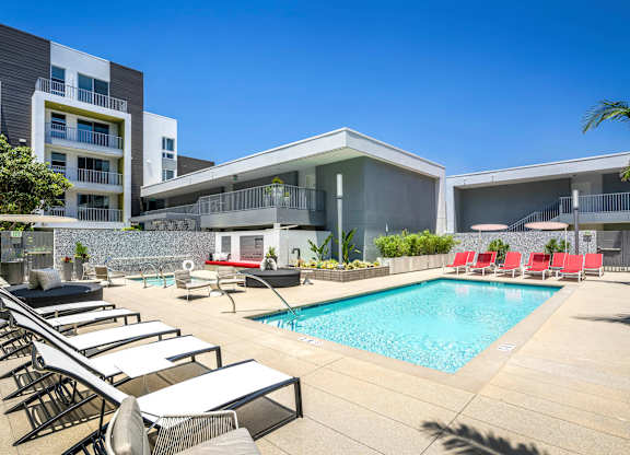 A pool area with sun loungers and a building in the background.