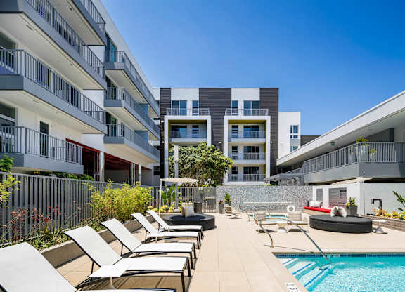 A pool area with sun loungers and a building in the background.